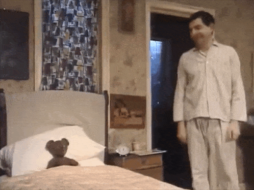 a man standing next to a bed with a teddy bear in it