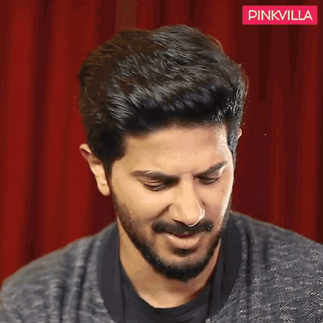 a man with a beard is making a funny face in front of a red curtain that says pinkvilla