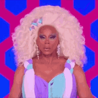drag queen rupaul is wearing a purple and blue dress and has a large blonde wig .
