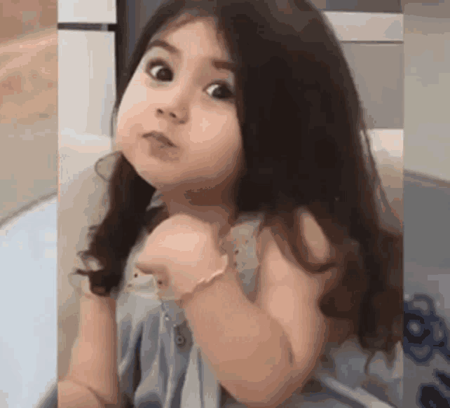 a little girl with long hair is sitting on a couch making a funny face .