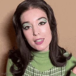 a woman in a green sweater and green eye shadow is smiling .