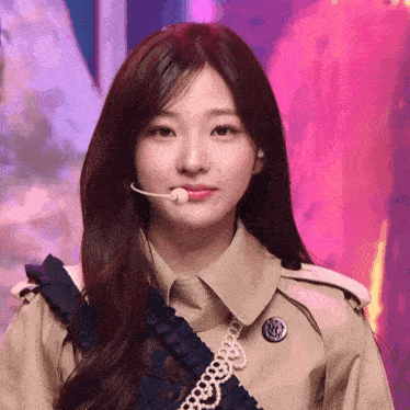 a woman wearing a trench coat has a microphone in her mouth and looks at the camera