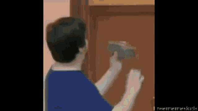 a man in a blue shirt is standing in front of a door holding a hammer .