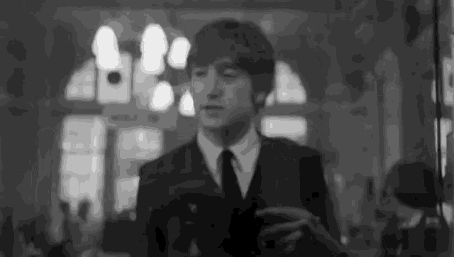 a black and white photo of a man in a suit and tie standing in front of a mirror .