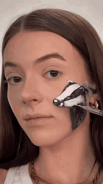 a woman has a badger painted on her face with a brush
