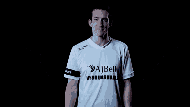 a man wearing a white ajbell unsquash shirt stands with his arms outstretched