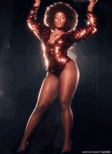 a woman in a red sequined bodysuit is dancing on a dark stage
