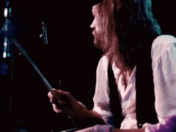 a man with long hair is playing a drum set in a dark room