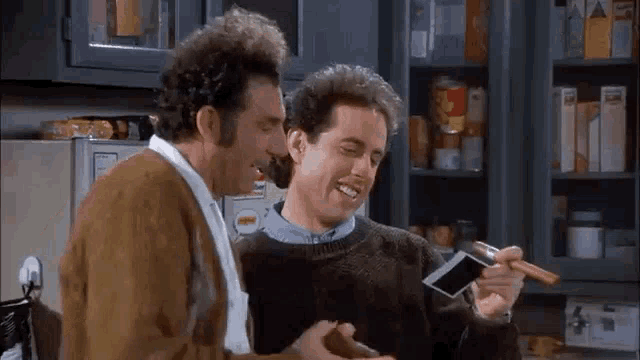 two men are standing next to each other in a kitchen . one of the men is holding a picture of a baby .