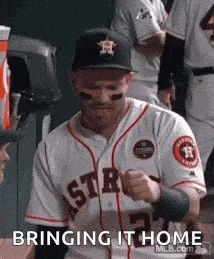 a baseball player is wearing a hat and a jersey and is sitting in the dugout .