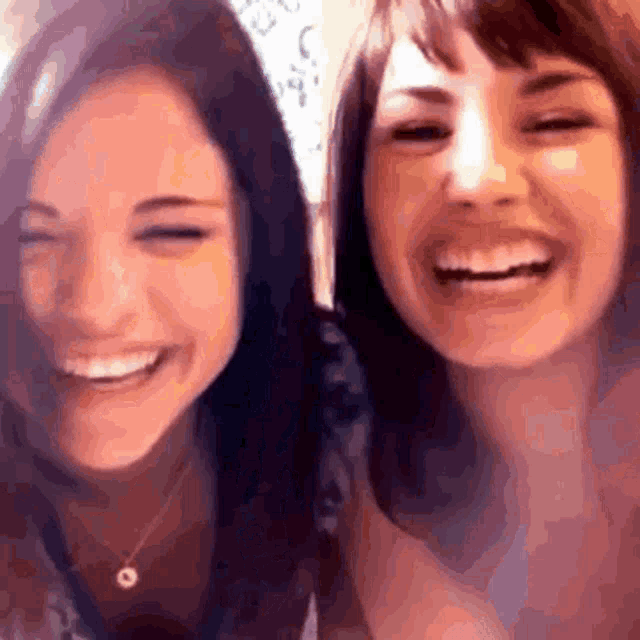 two women are smiling for the camera and one has a necklace with a circle on it