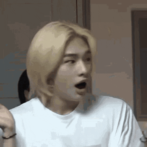 a young man with blonde hair is making a funny face with his mouth open .