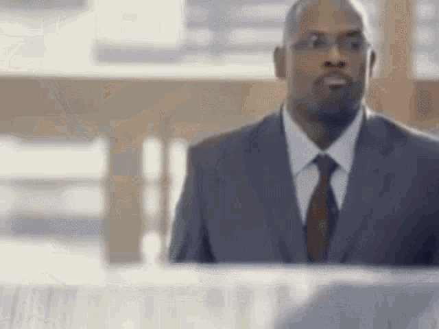 a man in a suit and tie is standing in front of a desk and looking at something .