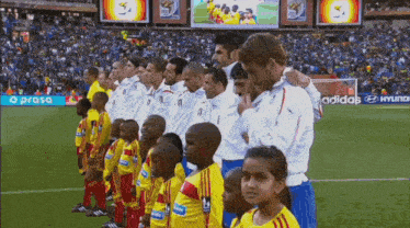 a group of soccer players stand on a field in front of a hyundai sign