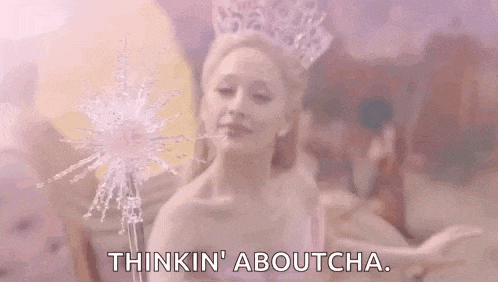 a woman in a crown is holding a magic wand and says `` thinkin ' aboutcha '' .