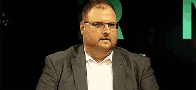 a man in a suit and glasses is sitting in front of a green letter n