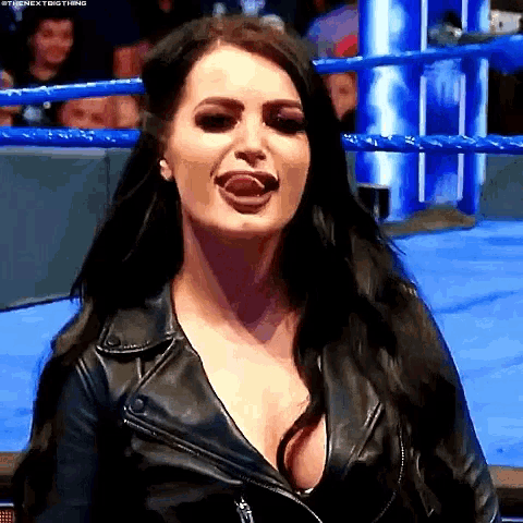 a woman in a leather jacket is sticking her tongue out while sitting in a wrestling ring .