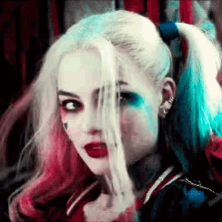 a woman in a harley quinn costume is holding a gun behind her face .
