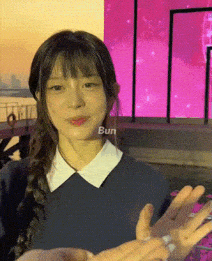 a girl with braided hair is holding someone 's hand in front of a pink background with the word bun on it
