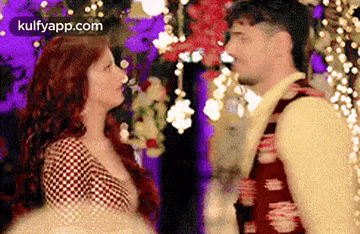 a man and a woman are looking at each other in a room with flowers in the background .