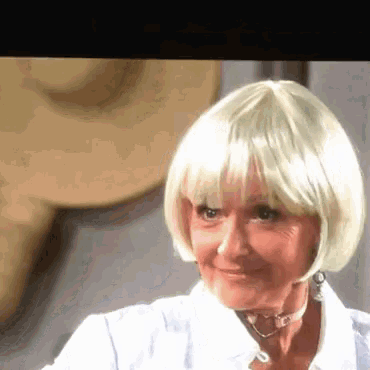 an older woman wearing a blonde wig and earrings is smiling .