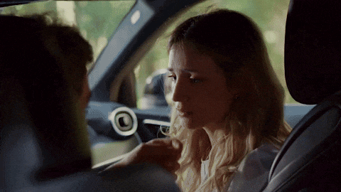 a woman is sitting in the driver 's seat of a car with a man holding her hand .