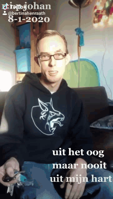 a man wearing glasses and a black shirt with a wolf on it is holding keys
