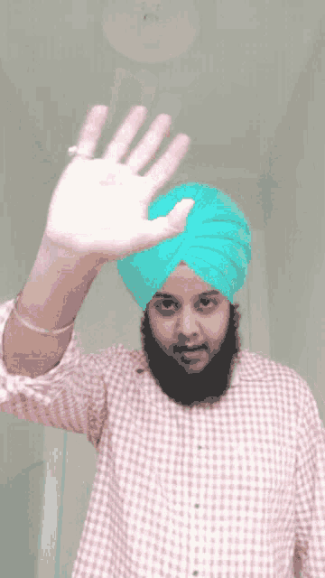 a man wearing a turban and a plaid shirt is waving his hand