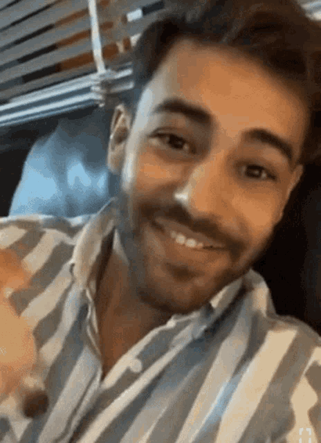 a man with a beard wearing a striped shirt is smiling