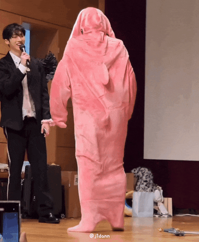 a man in a suit holds a microphone while standing next to a person in a pink bear costume