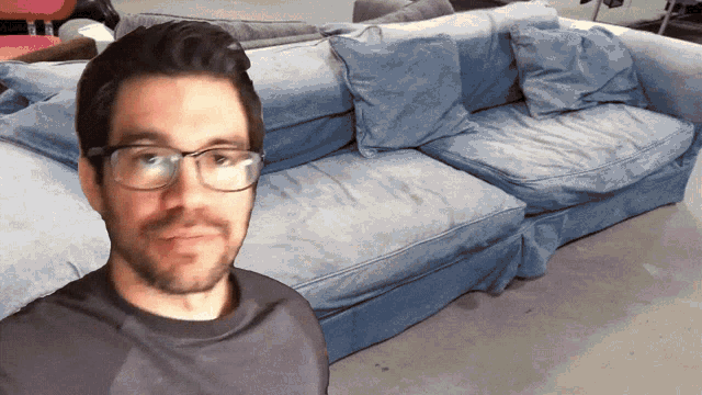a man wearing glasses stands in front of a couch