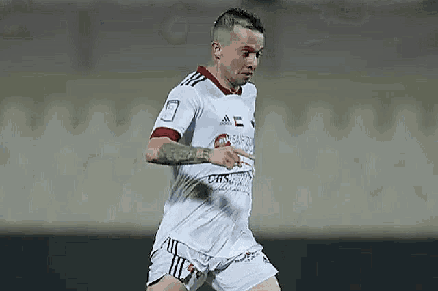a soccer player wearing a white jersey and shorts is running on a soccer field .