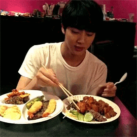 a man is sitting at a table eating food with chopsticks and a fork