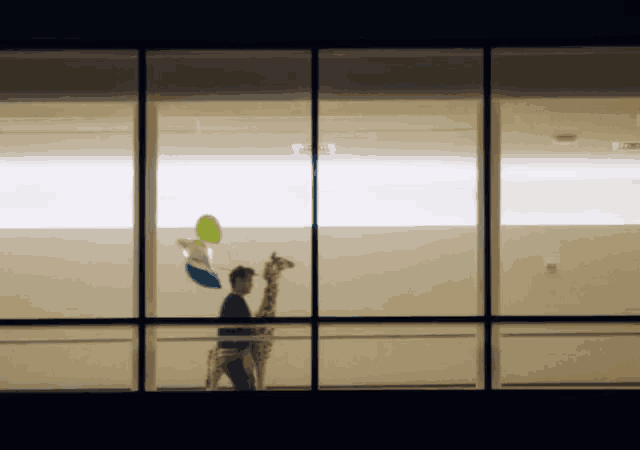 a man is holding a stuffed giraffe and balloons in front of a window