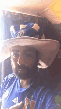 a man with a beard wearing a hat and a blue shirt with the letter u on it