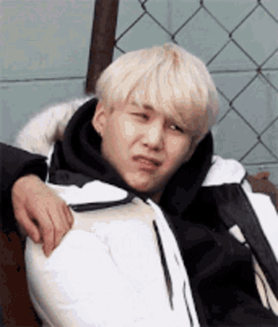 a young man with blonde hair is making a funny face while wearing a white jacket .