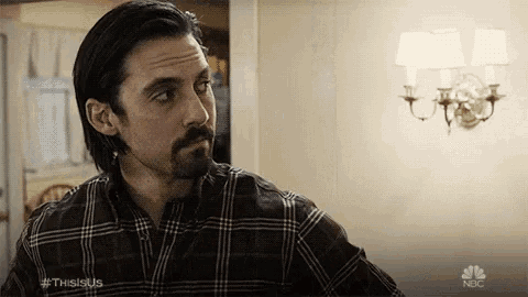 a man with a beard and mustache is wearing a plaid shirt and standing in front of a wall .