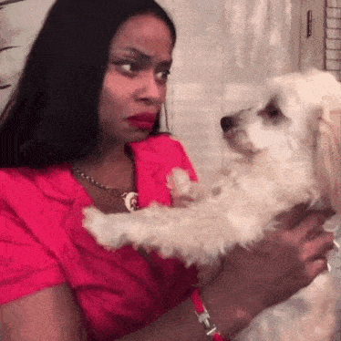a woman in a red shirt holds a small white dog in her arms