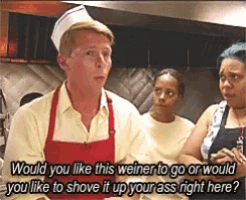 a man in an apron is talking to two women in a kitchen