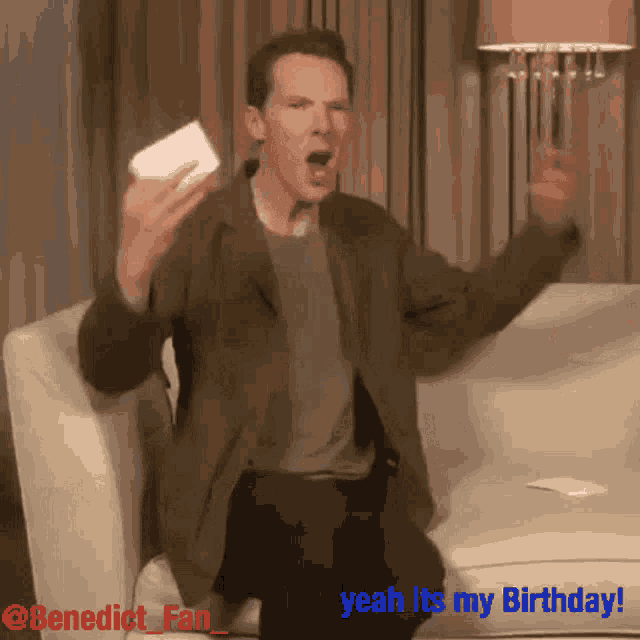 a man is sitting on a couch holding a piece of paper and saying " yeah its my birthday "