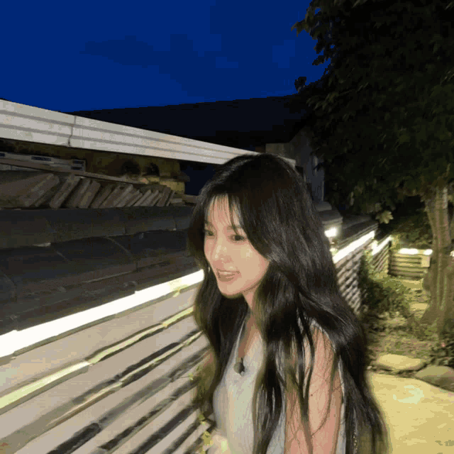 a woman with long black hair stands in front of a fence at night