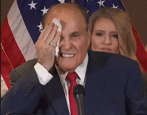 a man in a suit and tie wipes his face while a woman looks on