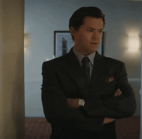 a man in a suit and tie stands with his arms crossed in a hallway