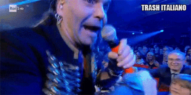 a man singing into a microphone with trash italiano written on the bottom right