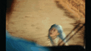 a blurry picture of a woman with blue hair standing in the sand .