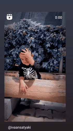 a little boy wearing a skeleton shirt is sitting on a wooden bench with his hand on his face
