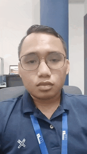 a man wearing glasses and a blue shirt has a lanyard around his neck that says iiu