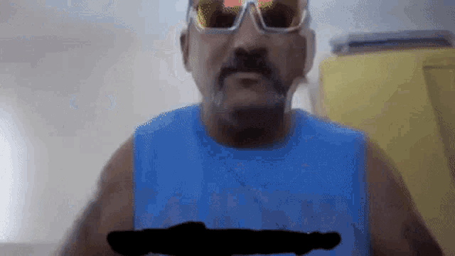 a man with a beard wearing sunglasses and a blue tank top has a black circle on his chest