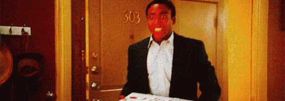 a man in a suit is holding a box of pizza in front of a door with the number 303 on it .