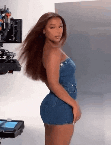 a woman in a denim dress is standing in front of a camera in a studio .